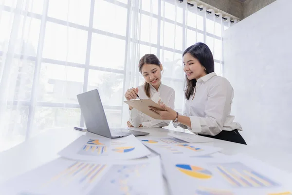 Two Asian businesswomen attending two Asian business partners discuss the financial and company planning graph during a budget meeting.