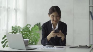 Asyalı kadın muhasebeci dizüstü bilgisayar ve akıllı telefon ile finansal grafik analizi üzerinde çalışıyor..