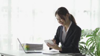 Asyalı kadın muhasebeci dizüstü bilgisayar ve akıllı telefon ile finansal grafik analizi üzerinde çalışıyor..