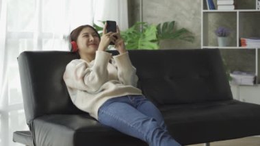 Sosyal medya, internet ve Asyalı kadınlar evdeki kanepede akıllı telefon kullanıyor. İnternet üzerinden alışveriş yapan ve telefonla mesaj gönderen bir kız.