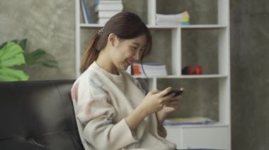 Sosyal medya, internet ve Asyalı kadınlar evdeki kanepede akıllı telefon kullanıyor. İnternet üzerinden alışveriş yapan ve telefonla mesaj gönderen bir kız.