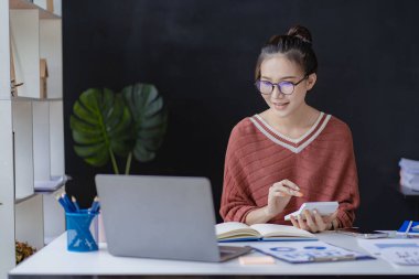 Masasında çalışan başarılı Asyalı kadın bilgisayarları ve serbest çalışanların finansal grafiklerini kullanarak gülümsüyor. Etrade Online Pazarlama Fikirleri