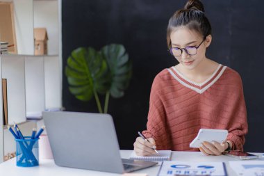 Masasında çalışan başarılı Asyalı kadın bilgisayarları ve serbest çalışanların finansal grafiklerini kullanarak gülümsüyor. Etrade Online Pazarlama Fikirleri