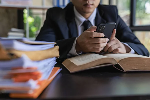 Young Asian businessman using a smartphone to work with a pile of paper on the table.Creative young man looking at a screen typing text messages with a smartphone. work from home concept