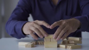 Genç Asyalı işadamı ahşap bloklardan bir kule inşa ediyor, emlak sektöründe büyüme kavramı.