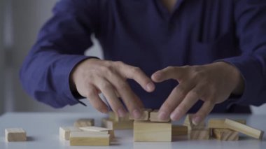Genç Asyalı işadamı ahşap bloklardan bir kule inşa ediyor, emlak sektöründe büyüme kavramı.