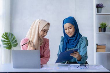 Ofiste finansal grafiklerle çalışan iki güzel Asyalı Müslüman kadın. Geleneksel giysili Müslüman iş kadını ofis toplantısında çalışıyor ve konuşuyor.