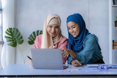 Ofiste finansal grafiklerle çalışan iki güzel Asyalı Müslüman kadın. Geleneksel giysili Müslüman iş kadını ofis toplantısında çalışıyor ve konuşuyor.