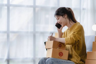 Asyalı bir kadın evinde kanepesinde oturmuş, bilgisayarı kutusuyla, başarılı Asyalı kadın elini kaldırmış, online pazarlama ambalaj ve teslimat kutusu, KME konsepti,