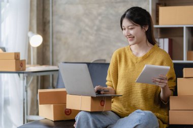 Asyalı bir kadın evinde kanepesinde oturmuş, bilgisayarı kutusuyla, başarılı Asyalı kadın elini kaldırmış, online pazarlama ambalaj ve teslimat kutusu, KME konsepti,