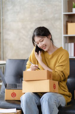 Asyalı bir kadın evinde kanepesinde oturmuş, bilgisayarı kutusuyla, başarılı Asyalı kadın elini kaldırmış, online pazarlama ambalaj ve teslimat kutusu, KME konsepti,