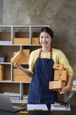 Çevrimiçi dağıtım konsepti, siparişi kontrol ederken kutuya gülümseyen kadın. Serbest çalışanlar ya da satış elemanları üretim ambalajlarını inceliyor. KOBİ 'ler evdeki kutular üzerinde çalışıyorlar.