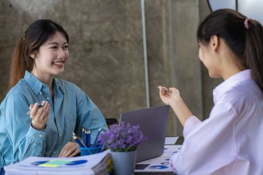 İki genç Asyalı kadın yeni bir başlangıç projesi konseptini tartışıyor. Dizüstü bilgisayarlarda finansal planlama, istatistik ve yatırım pazarının analizi