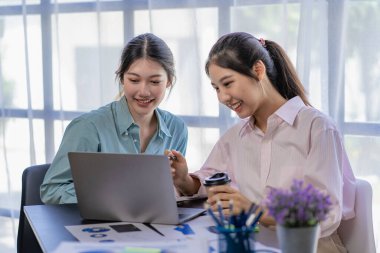 İki genç Asyalı kadın yeni bir başlangıç projesi konseptini tartışıyor. Dizüstü bilgisayarlarda finansal planlama, istatistik ve yatırım pazarının analizi