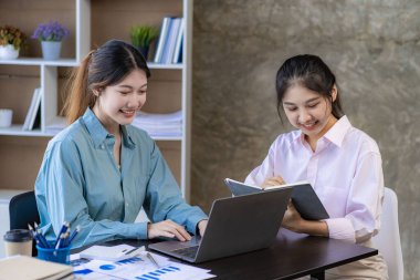 İki genç Asyalı kadın yeni bir başlangıç projesi konseptini tartışıyor. Dizüstü bilgisayarlarda finansal planlama, istatistik ve yatırım pazarının analizi