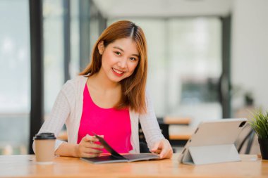 Asyalı kız öğrenciler, tabletle online e-öğrenim görüyorlar masada oturuyorlar ve kafeteryada kalem mesafesi öğrenme konsepti tutuyorlar.