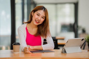 Asyalı kız öğrenciler, tabletle online e-öğrenim görüyorlar masada oturuyorlar ve kafeteryada kalem mesafesi öğrenme konsepti tutuyorlar.