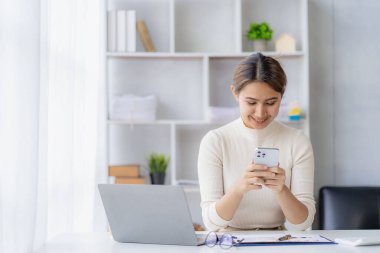 Başarılı bir Asyalı iş kadını akıllı telefonuyla gülümseyip finansal muhasebe konsepti şirketinin ofisindeki bir müşterisiyle konuşuyor..