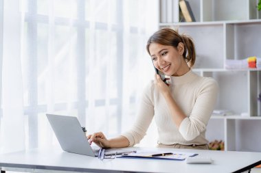 Başarılı bir Asyalı iş kadını akıllı telefonuyla gülümseyip finansal muhasebe konsepti şirketinin ofisindeki bir müşterisiyle konuşuyor..