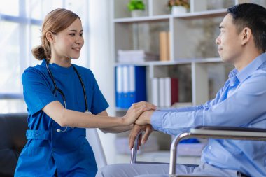Asyalı kadın doktorlar, hastane ve klinik konseptinde danışma ve sağlık kontrolünden sonra tekerlekli sandalyedeki erkek hastaları teşvik eder ve desteklerler.