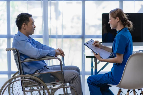 アジアの女性医師は 診療所の概念で健康診断を受けた後 車椅子の男性患者を奨励し サポートします — ストック写真