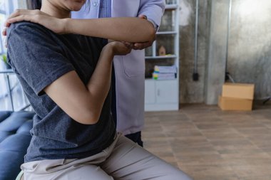 Bir doktor ya da fizyoterapist yaralı kolu muayene eder. Klinikte acı psikoterapisi uygulanıyor.