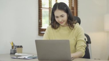 Bilgisayarda çalışan Asyalı kadın dizüstü bilgisayara bakıyor evde dinleniyor internet iletişim sistemi üzerinden çalışıyor.