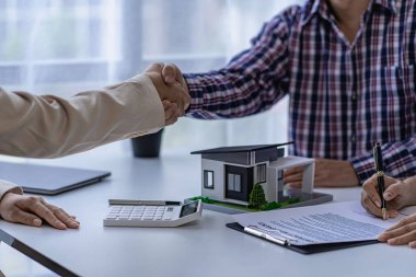 Bir emlakçı, bir ev almak ya da emlakçının ofisinde kiralamak için kontrat imzaladıktan sonra müşteriyle el sıkışır..