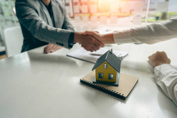 A home agent shakes hands with a customer after signing a contract to buy a home or rent it in the real estate agent's office.