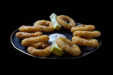 Limonlu siyah tabakta kızarmış mürekkep balığı halkaları. Seçici odak noktası.