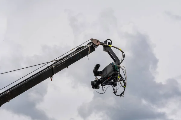 cinema and television camera suspended on a broadcast crane with the cloudy sky in the background