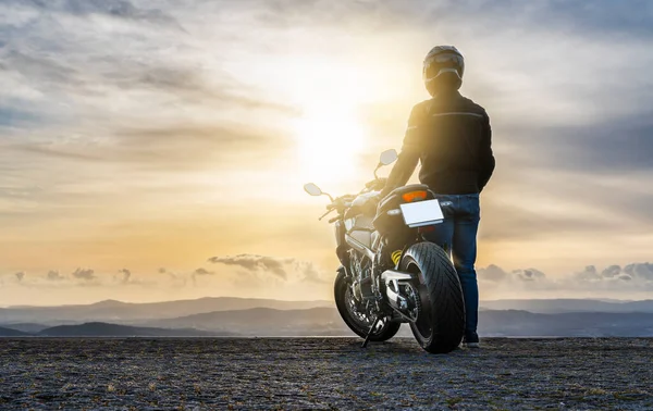 Motorcu motosikletin yanında duruyor, gün batımını izliyor - kopyalama alanı