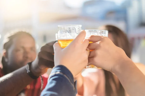 Happy people toasting with beer at brewery bar out doors - Young friends having fun together at happy hour - focus on glass