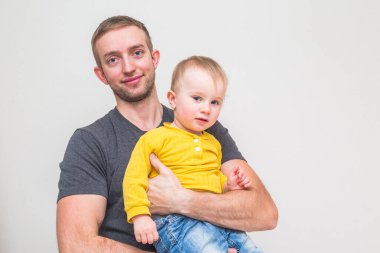 Bir yıl ve üç aylık çocuk babasının kollarında beyaz duvar arkasında.