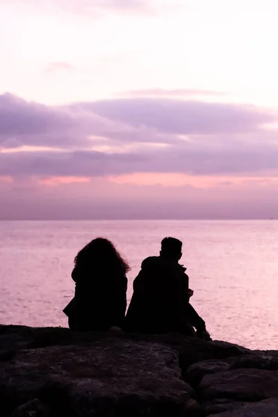 Shadow of couple sitting on the rocks close to the sea at night