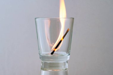 Işık arkaplanındaki şeffaf bir camda yanan kibrit