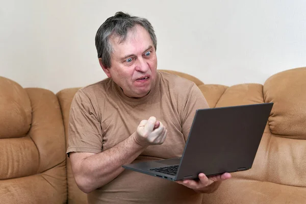 Мужчина в возрасте, сидящий на Дэвани, просматривает новости на ноутбуке. — стоковое фото