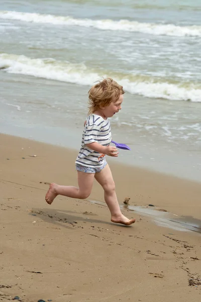 Un bambino corre lungo la spiaggia di sabbia lungo la riva del mare — Foto Stock