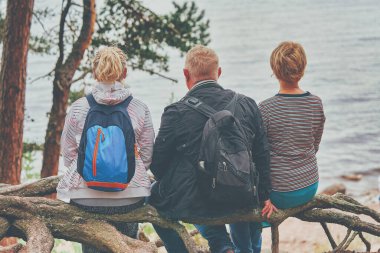 Bir adam ve iki kadın bir orman gölünün kıyısında oturuyor.