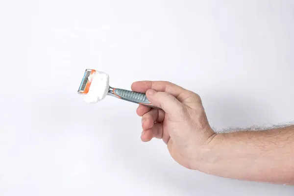 La mano sostiene una afeitadora con espuma de afeitar sobre un fondo blanco —  Fotos de Stock