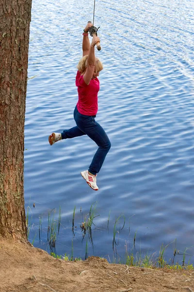 Vrouw van middelbare leeftijd in sportkleding hangend aan een stok met een touw boven het water — Stockfoto