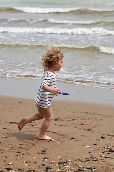 Un petit garçon court le long de la plage de sable le long du littoral — Photo