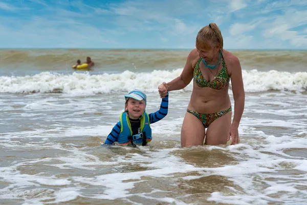 Μια γυναίκα παίρνει ένα παιδί με σωσίβιο από την φουρτουνιασμένη θάλασσα. — Φωτογραφία Αρχείου