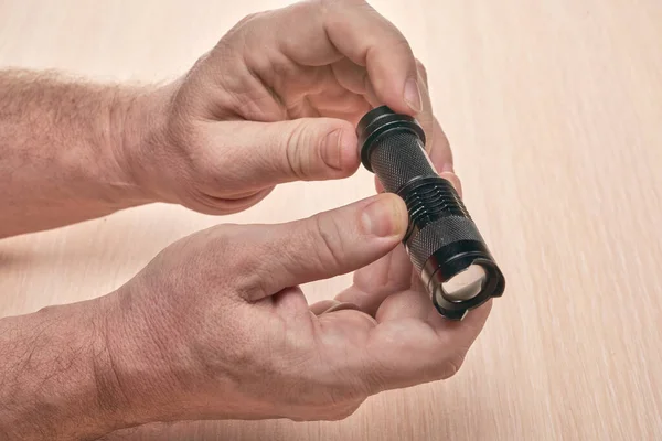 Hände halten eine kleine schwarze Taschenlampe, um den gebrauchten Akku zu ersetzen — Stockfoto