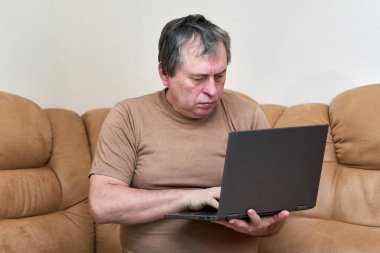 Devani 'nin üzerinde oturacak yaşta bir adam haberlere dizüstü bilgisayarla bakıyor..