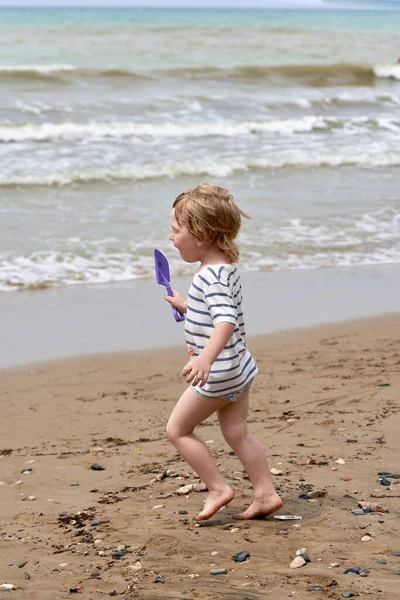 Un bambino corre lungo la spiaggia di sabbia lungo la riva del mare — Foto Stock