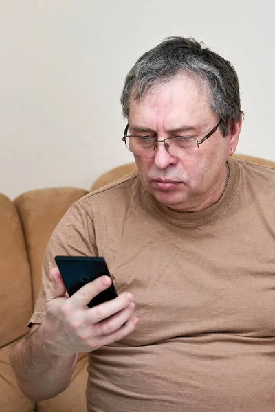 Ηλικιωμένος πολίτης κάθεται στον καναπέ καταλαβαίνει το gadget, mastering smartphone — Φωτογραφία Αρχείου