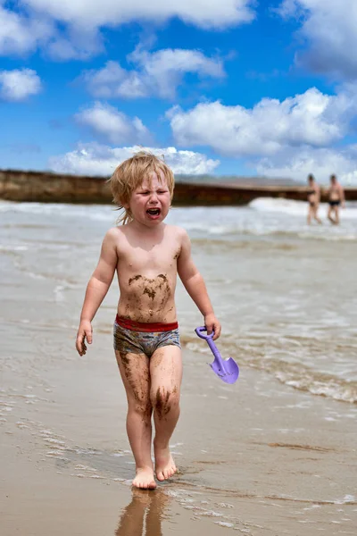 Ένα μικρό αγόρι λερώνεται στη λάσπη και περπατάει κλαίγοντας στην παραλία — Φωτογραφία Αρχείου