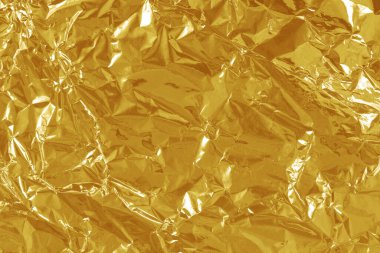 Altın folyo yaprağının parlak dokusu, arkaplan ve tasarım çalışmaları için soyut sarı ambalaj kağıdı.