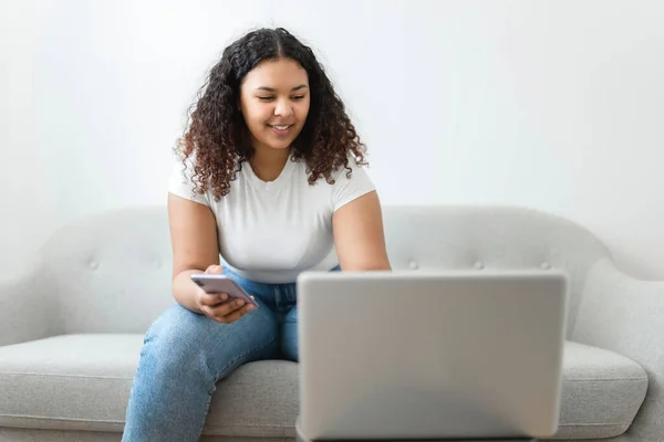 Ung afrikansk amerikansk kvinde med bærbar computer derhjemme med kreditkort på hånden - Stock-foto